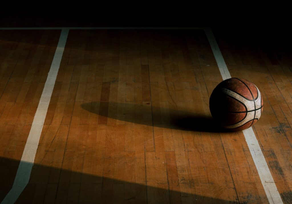A basketball resting on a parquet court in a dimly lit gym creates a moody sports scene.
