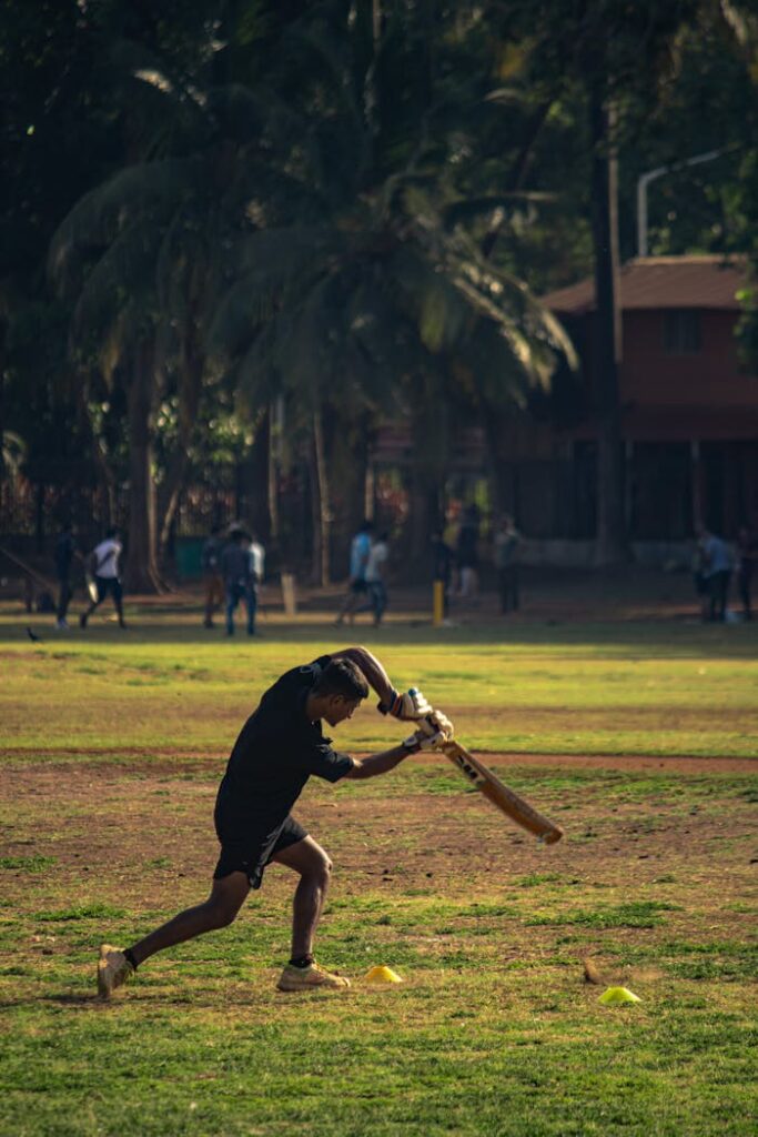 A young man actively playing cricket on a sunny day in a rural setting.