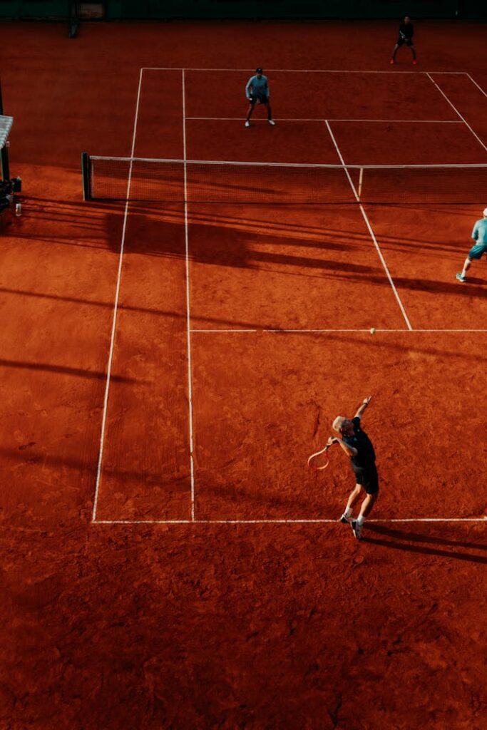 Overhead view of a tennis match on a clay court with four players competing in doubles.