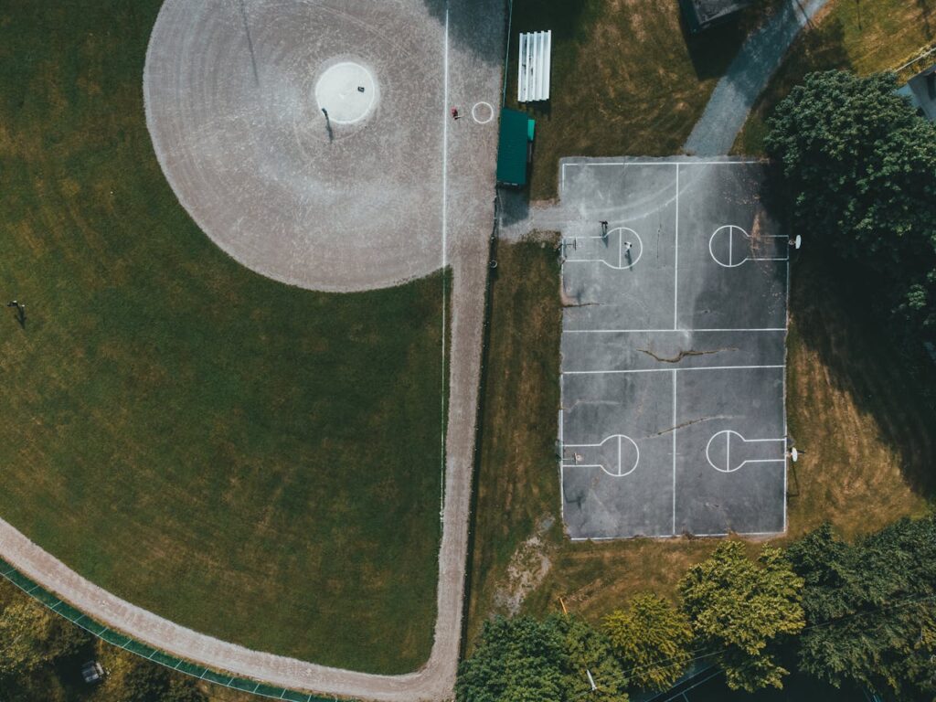 Aerial view of a park featuring a basketball court and baseball field surrounded by greenery.